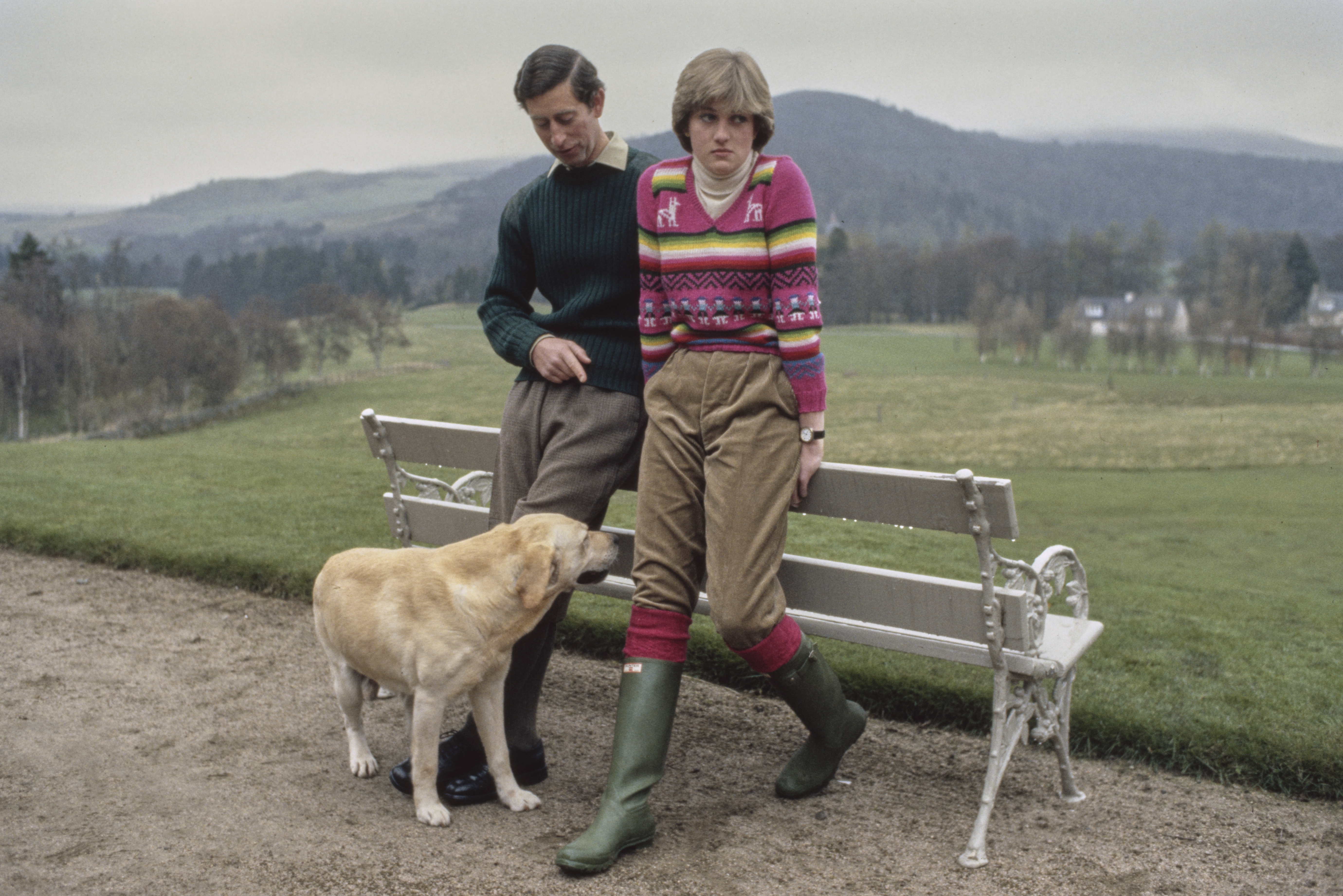 Princess Diana wearing a pink sweater and Prince Charles posing on a bench in Balmoral, Scotland