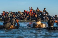 Migrants wade in deep water to board a dinghy into the English Channel on August 25, 2025 in Gravelines, France.