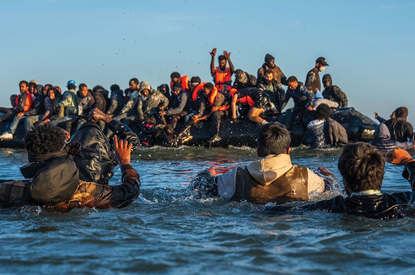 Migrants wade in deep water to board a dinghy into the English Channel on August 25, 2025 in Gravelines, France.