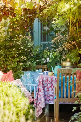 outside seating area with tablecloth and cushions under a vine outside a converted barn