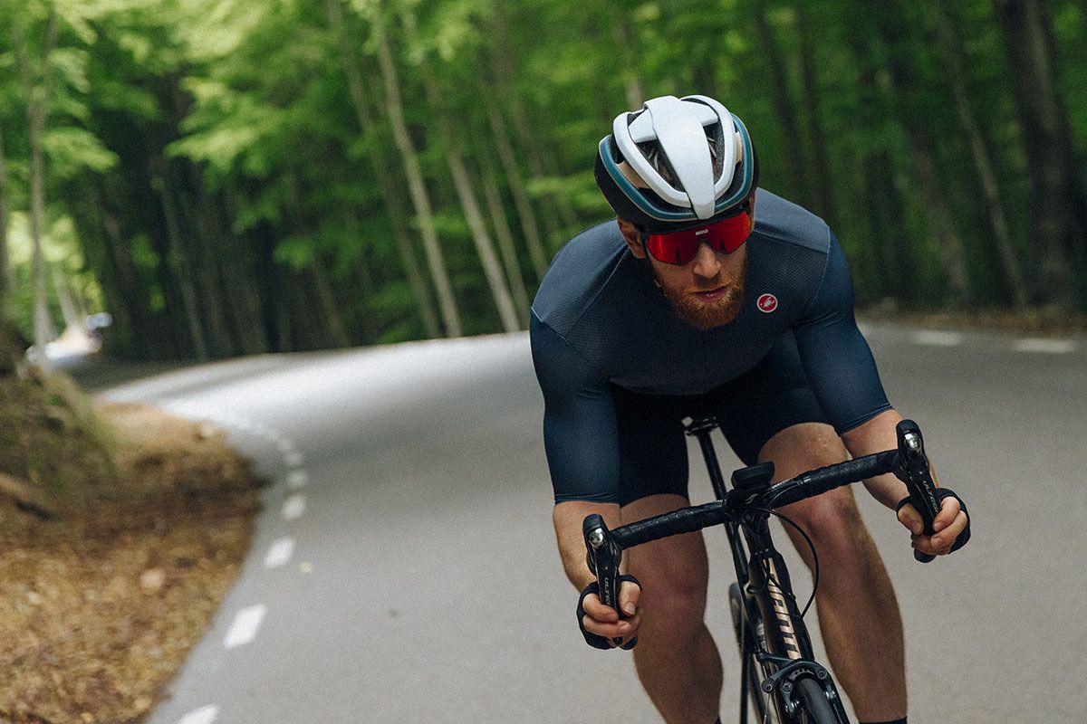 Rider cycling on the drops, descending on a winding road wearing a white HJC helmet and blue castelli jersey 