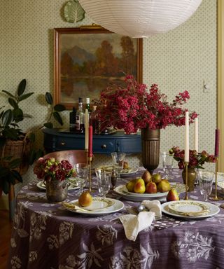 holiday table setting with purple tablecloth, vase of red flowers and long taper candles