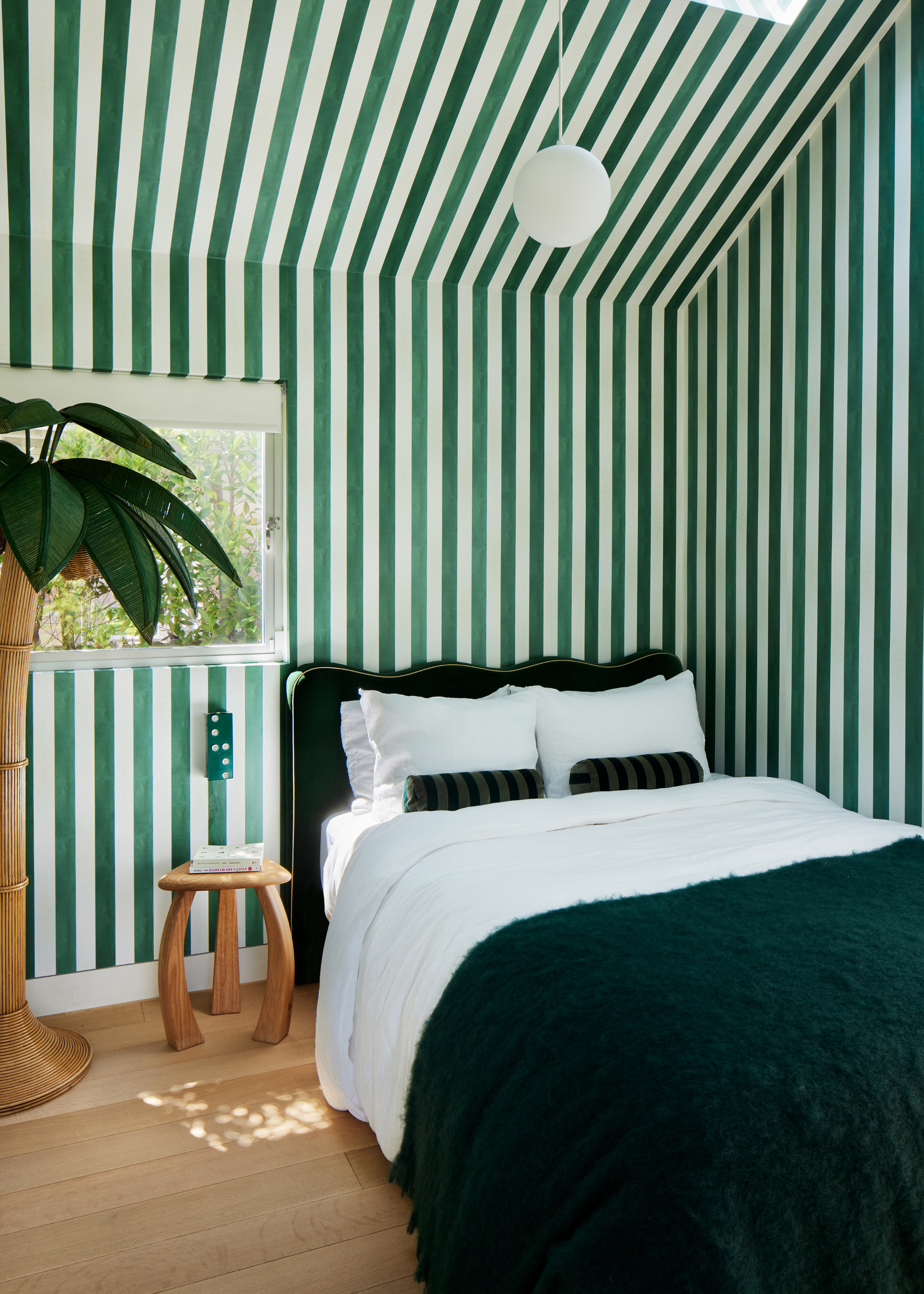 A bedroom with green and white striped wallpaper and a green bedscape by a wood side table