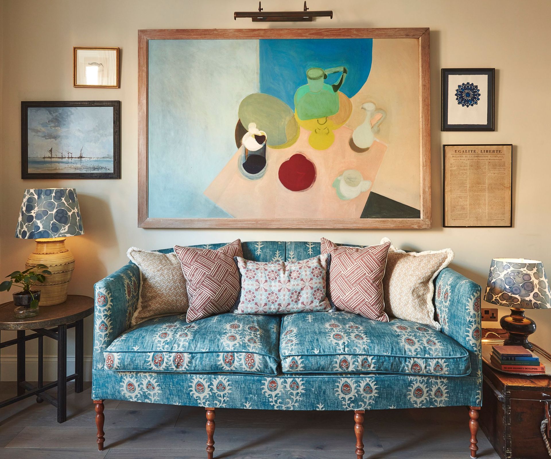 Eclectic living room with upholstered sofa and patterned cushions, side tables with printed lampshades and large abstract still life painting