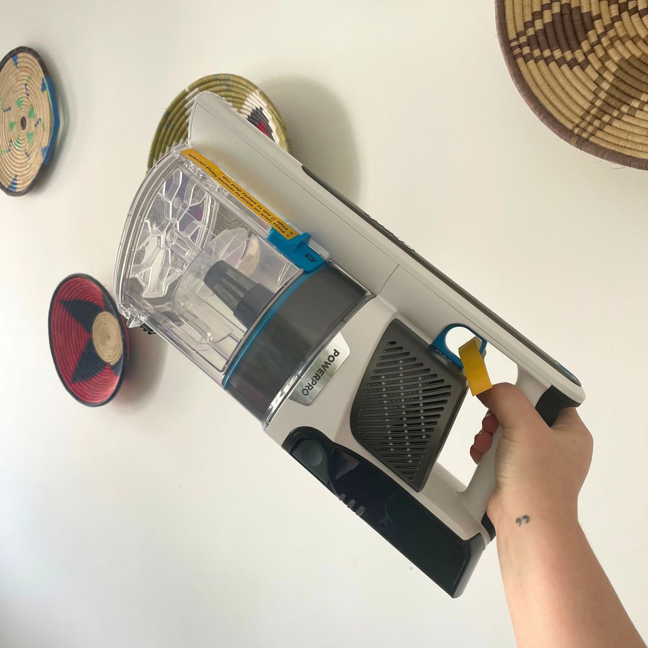 Shark PowerPro Pet Cordless Stick Vacuum handheld being held up in front of a white wall with colourful baskets on it