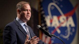 a white man in a suit talks into a microphone