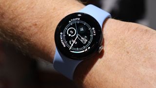 En Google Pixel Watch 2 med ett ljusblått armband runt en handled.