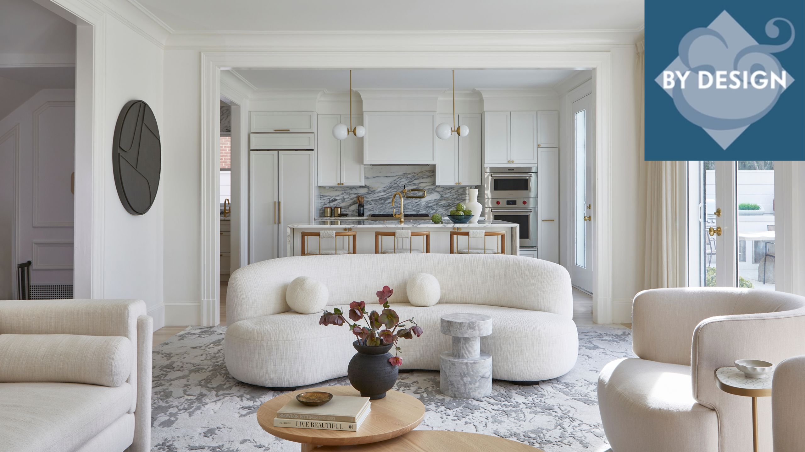 White and cream minimalist living room with curvacous sofa andn chairs, marble and white minimal kitchen in background