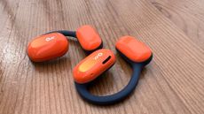 The Oladance open ear headphones in bright orange on a wooden surface 