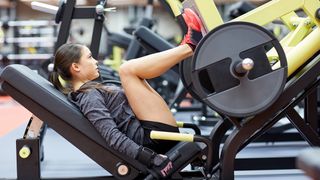 Woman preforming leg press on weights machine in gym