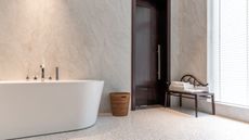 A modern style bathroom with a large white bath and travertine style wall tiles