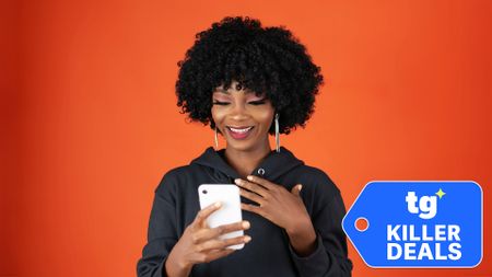 Woman looking at phone while smiling against an orange background