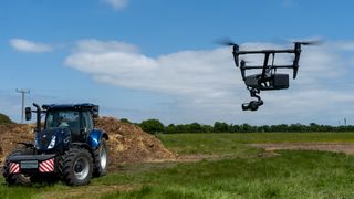 DJI Inspire 3 flying in a field toward a blue tractor and a pile of manure