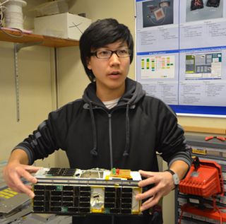 A student holds CINEMA, the CubeSat for Ions, Neutrals, Electrons & MAgnetic fields, an 8-pound, shoebox-size package. A similar type CubeSat could carry out lunar exploration in the future.