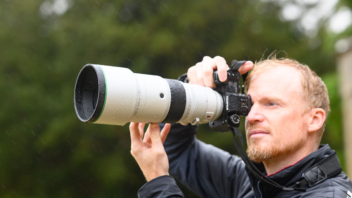 TechRadar Cameras Editor Tim Coleman holding the Fujifilm XF 400mm F4.5 R LM OIS WR telephoto prime lens attached to a Fujifilm X-H2S camera, out in the rain taking pictures