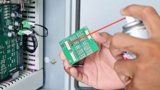 close up of a person's hands using a dust spray to clean a computer chip