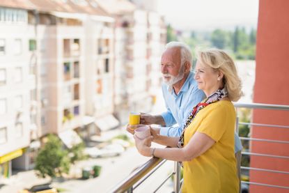 Senior couple drinking coffee on a balcony in a city.