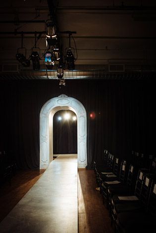 a white moulded archway framing the models' entrance onto a cream runway. Set upon aged wooden flooring