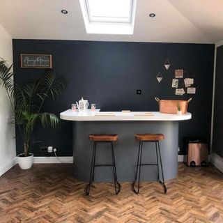 A stand alone bar area in front of a black feature wall in a white kitchen with white parquet flooring