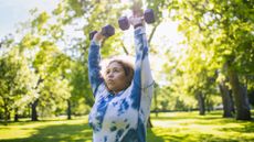 Woman doing push press overhead with dumbbells outside in a park
