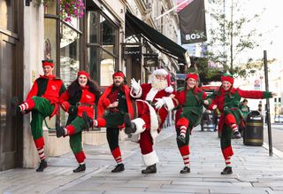 Hamleys Father Christmas and elves doing a funny walk in a row down a London street