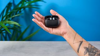 a pair of silver and black shiny earbuds with a black matte charging case are photographed against the Tom's Guide blue background