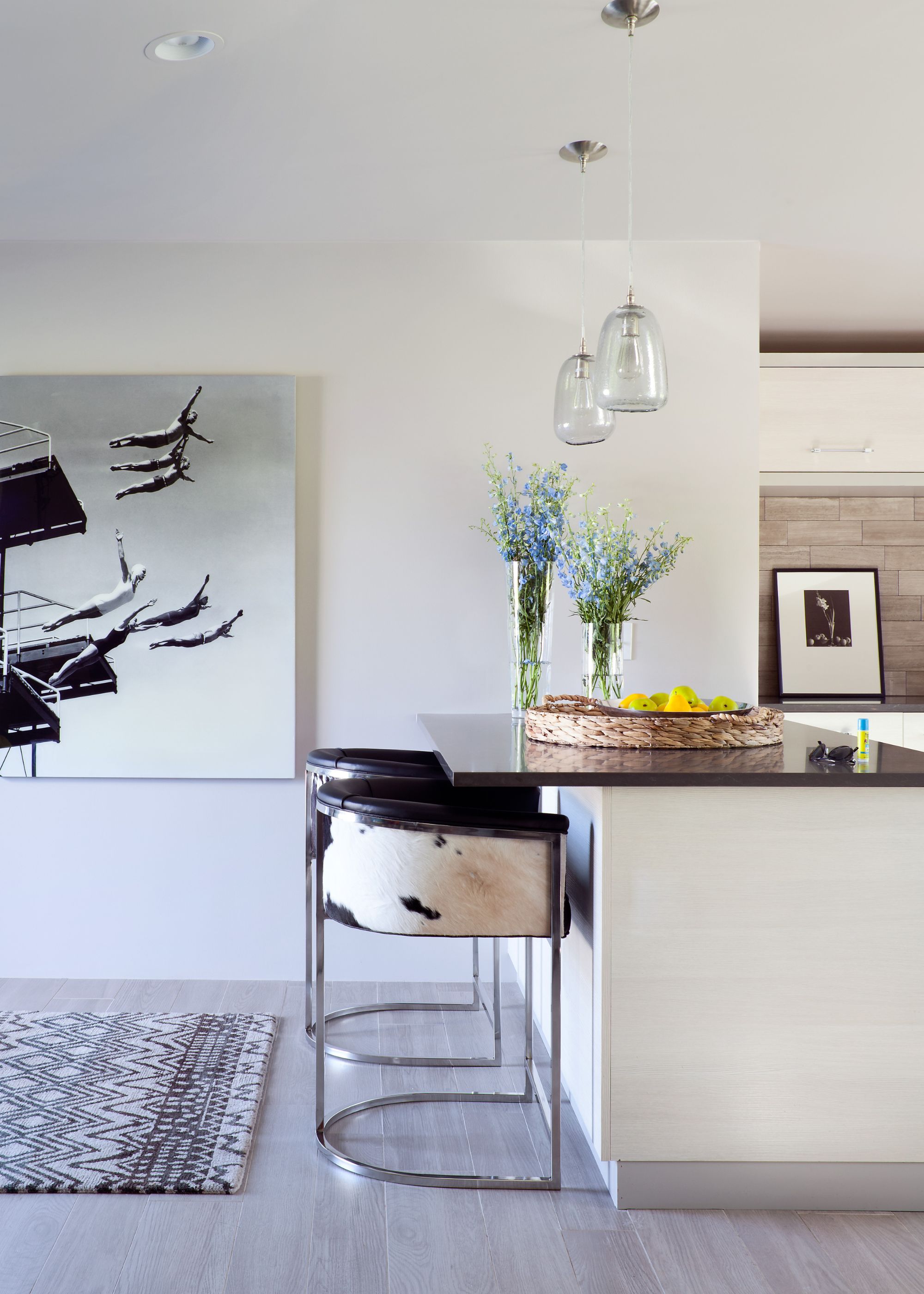 Cow print bar stools with a large island in the kitchen. Above the island are two hanging pendant lights and on the island are vases with flowers inside of them.