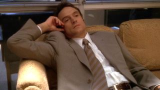 Josh Lyman (Bradley Whitford) lounges on an office couch on The West Wing. 