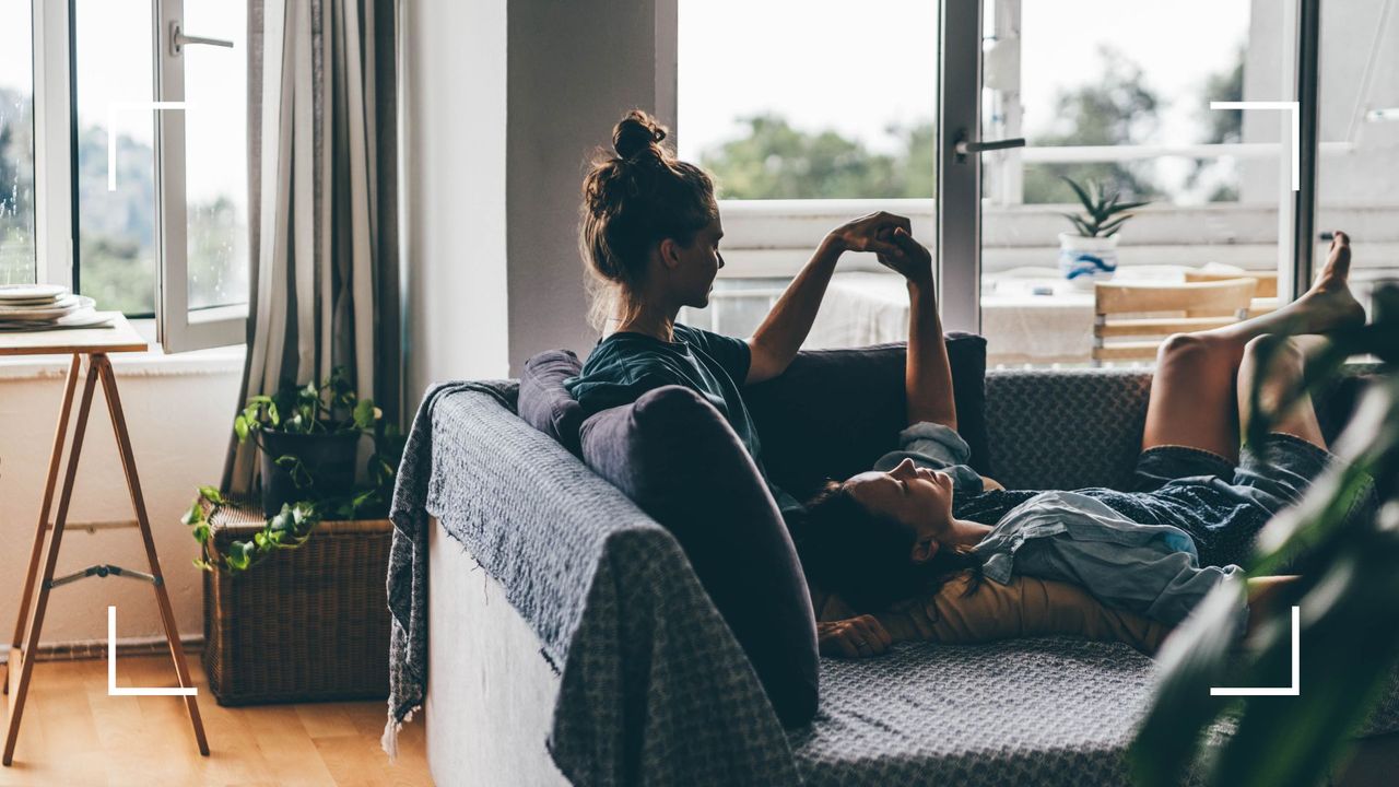 Two women lying on the sofa together with daylight coming through the window, representing the sniper sex position