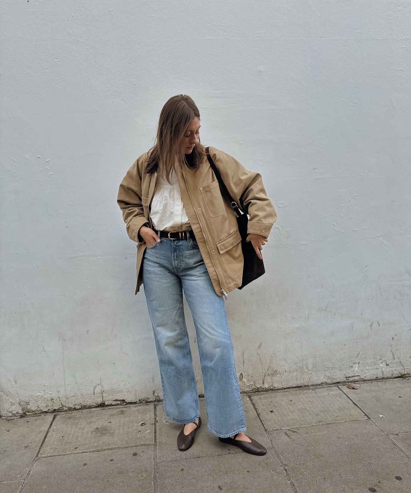 Woman wears beige jacket, blue jeans and ballet flats