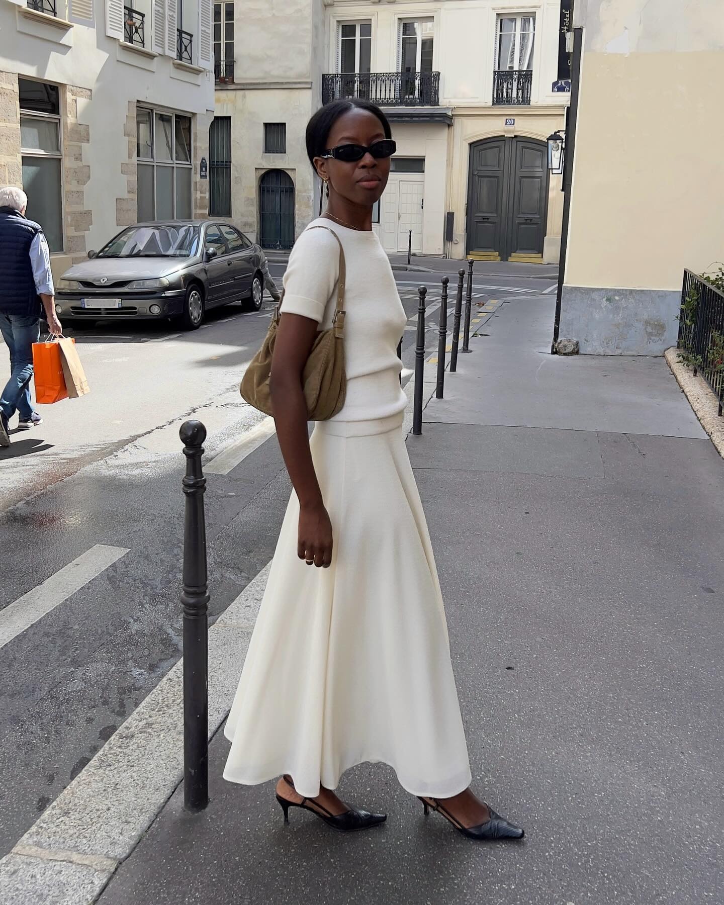 French woman wearing a white maxi skirt, white T-shirt, black heels and a brown bag.