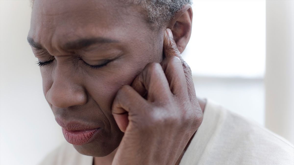 close up of a woman&#039;s face as she winces and holds a finger to one ear, as if trying to tune out a noise