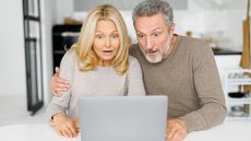 Surprised middle-age couple received unexpected news, mature husband and wife staring at the laptop screen with mouths open and astonished faces expression