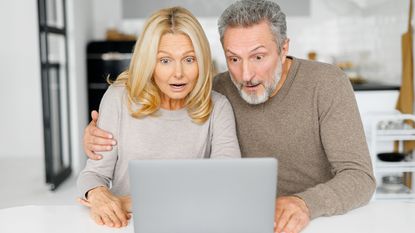 Surprised middle-age couple received unexpected news, mature husband and wife staring at the laptop screen with mouths open and astonished faces expression