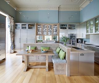 large kitchen diner with brushed chrome appliances and a built in seating area with green cushions and wooden table