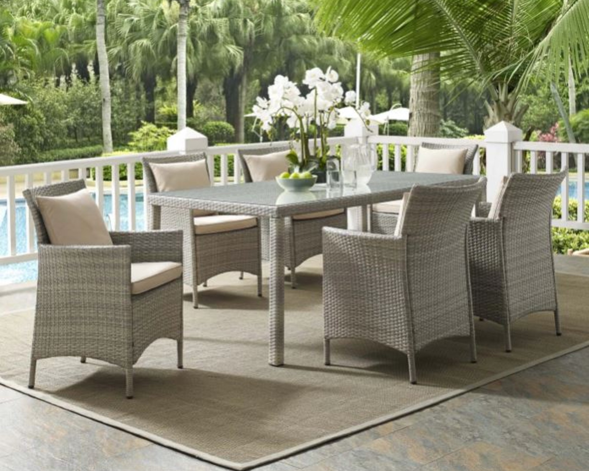 A rattan dining set on a balcony overlooking a pool