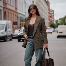 A woman walks along a Paris street wearing jeans and a check blazer.