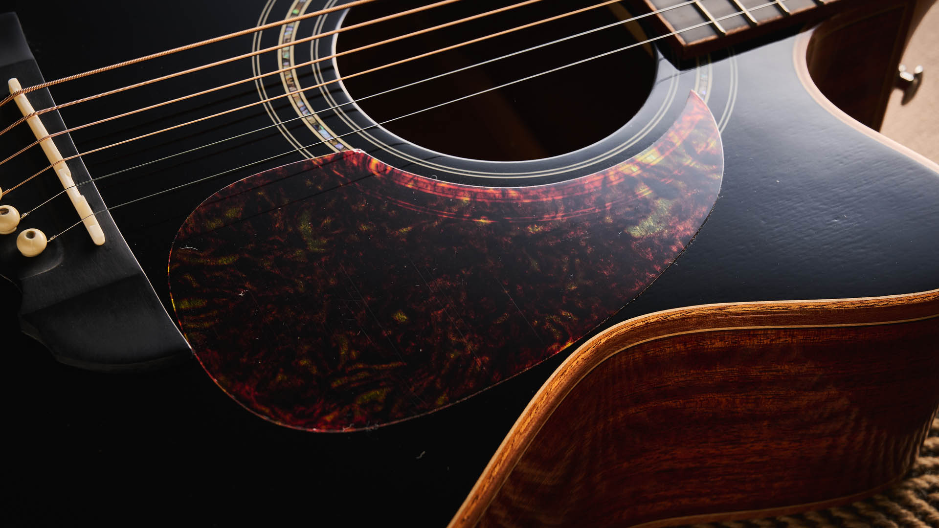 Harley Benton CLC-650SM-CE: the affordable cutaway electro-acoustic has a black top, natural back and sides, with an attractive arm-rest and tortoiseshell pickguard, and is here photographed against a wooden floor.