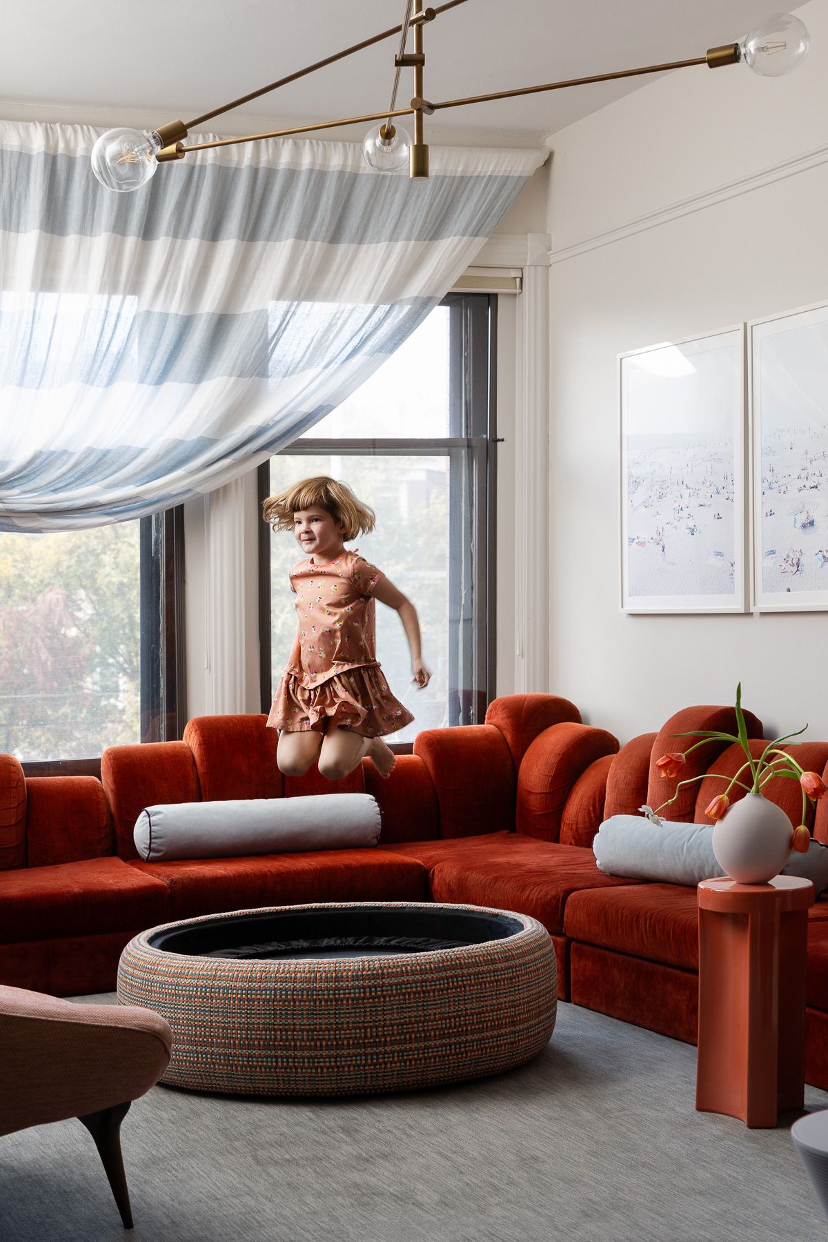 A family room with a large, red couch, a gray carpet and three small stools in varied colors
