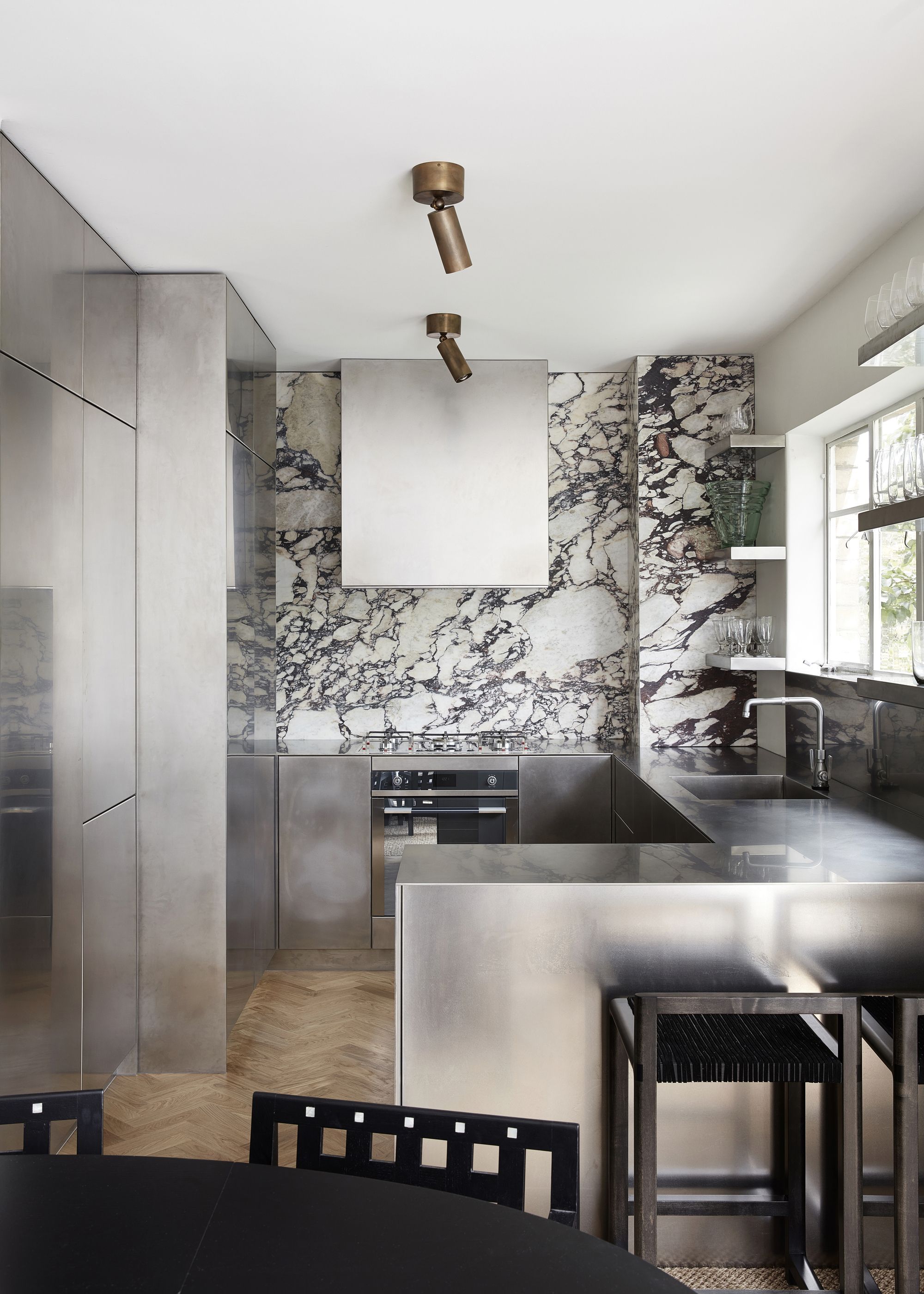 A stainless steel kitchen with stainless steel worktops and cabinets as well as a contrasting marble backsplash