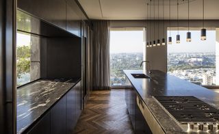 A kitchen with a large black marble island, storage, stove, pendant lights, wooden floors and a large sliding door.