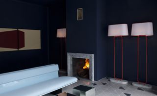 Casa Fayette reception with navy blue walls, marble fireplace, tall red lamps with white shades and grey bench