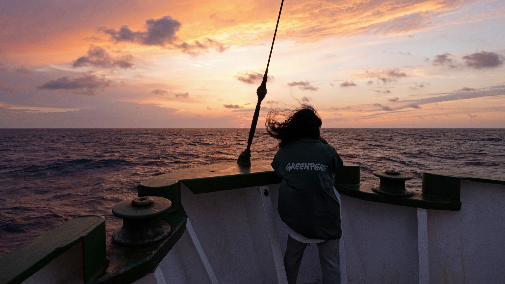 The Greenpeace ship Arctic Sunrise sailing at sunset, with a female volunteer facing out to sea