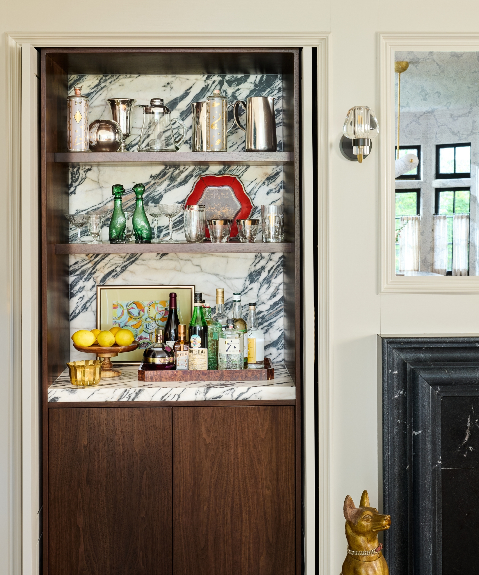 A kitchen alcove transformed into a home bar with dark wood cabinetry, a marble counter and backsplash, silver shelves, and pocket doors