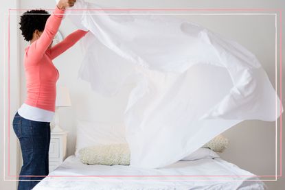 A woman shaking a sheet over a bed