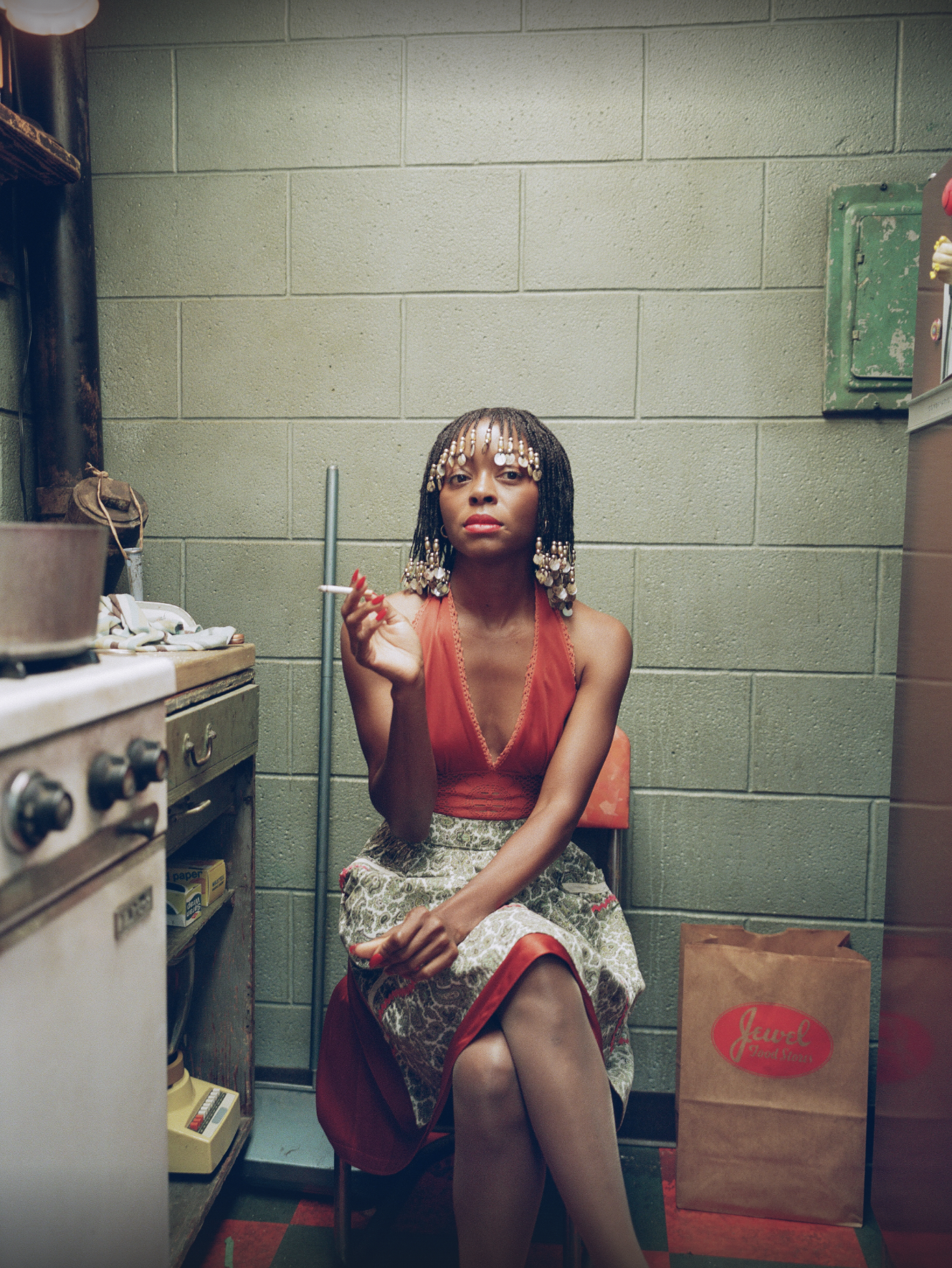 danielle deadwyler in a red body suit and skirt sitting on a chair in an old kitchen in euphoria season 3