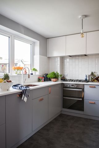 a modern kitchen with grey cabinets, white wall tiles and copper handles