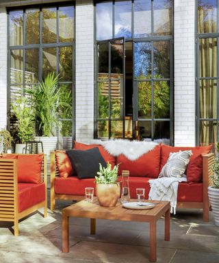 A wooden outdoor furniture set with red/orange upholstered outdoor cushions and faux fur decor