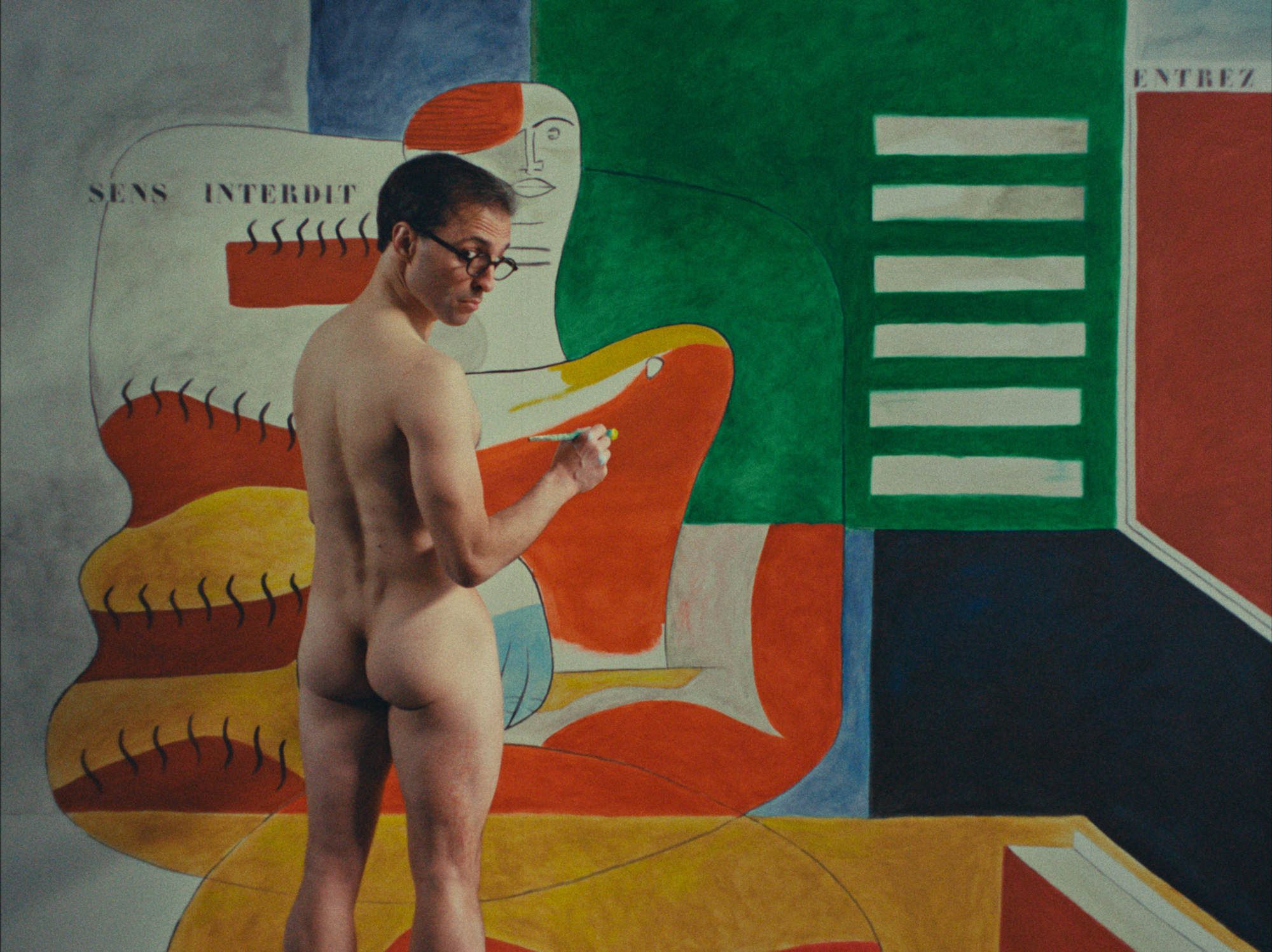 a scene from the film E.1027 – Eileen Gray and The House by The Sea depicting le corbusier painting on the walls in the nude