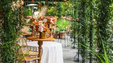 Garden party setting with high tables and chairs. orange floral arrangements and greenery